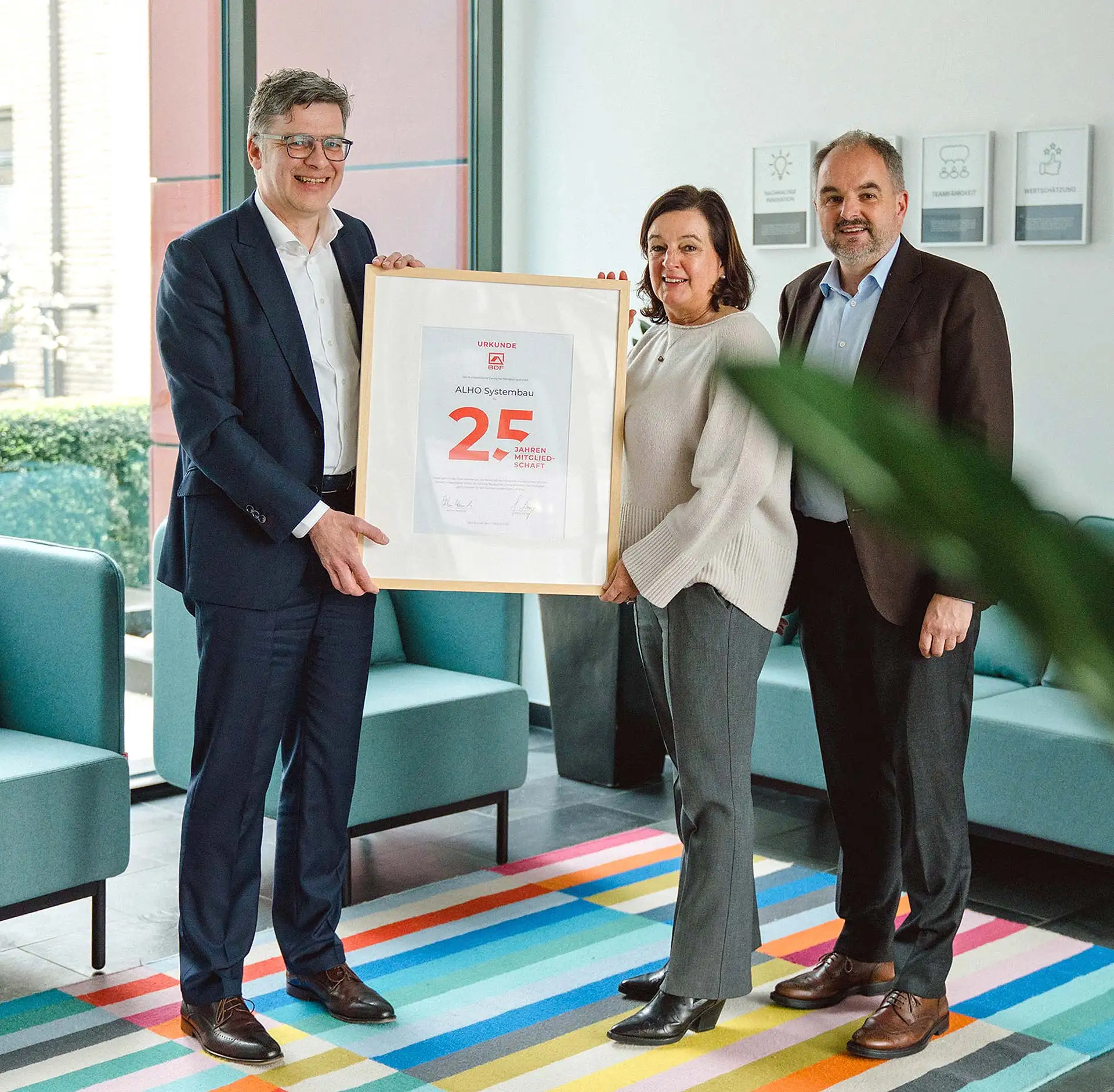 Im Namen der ALHO-Inhaberfamilie nahmen Silvia Matschke (m.), Geschäftsführung FAGSI Vertriebs- und Vermietungs-GmbH, und Achim Holschbach (r.), Geschäftsführung ALHO Holding GmbH, jetzt die Jubiläumsurkunde von BDF-Geschäftsführer Georg Lange (l.) entgegen. Foto: ALHO Systembau
